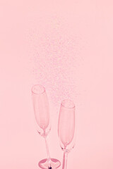 Two chrystal champagne glasses with heart shaped confetti on pastel pink background. Minimal style.