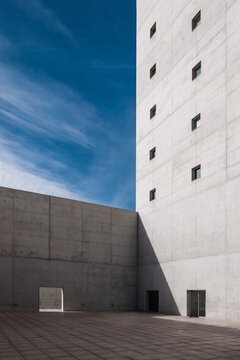 Facade of gray monolithic brutalist building with tiny windows and gate in tall concrete barrier