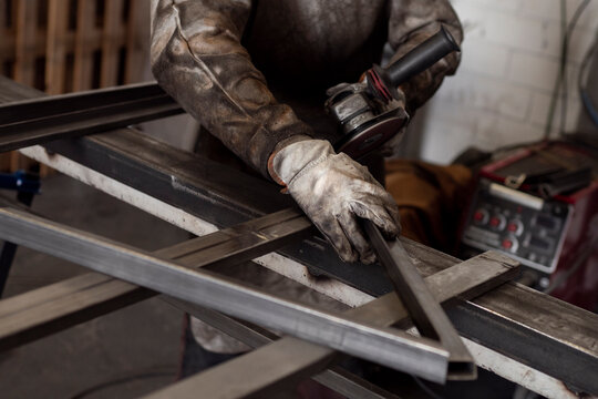 Crop of male worker in dirty apron standing at workbench and preparing metal details for welding