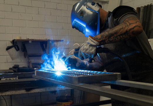 Unrecognizable male welder using welding machine on metal detail while working at workbench in factory