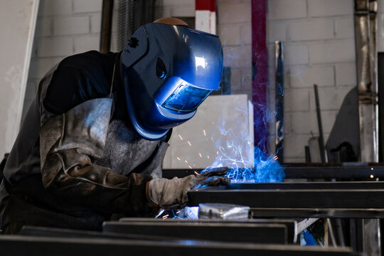 Unrecognizable male employee in protective gloves and helmet using welding machine while working in dark workshop