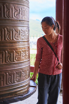 Full body of Asian female passing by Tibetan rolls with ancient prayer near sacred oriental temple