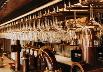 Interior of bar with shiny glasses hanging on metal rack over draught beer taps in restaurant In Madrid