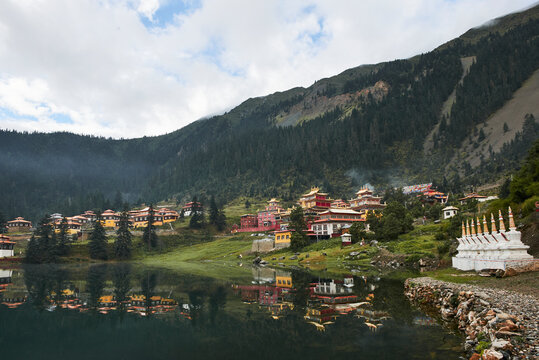 Scenery view of old buildings of Tibetan Buddhist temples located on shore of tranquil reflecting lake in highland covered with clouds