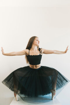 Graceful Female Ballet Dancer Wearing Black Tutu Standing In Pointe Shoes On Tiptoes In Dance Position On White Background And Looking Away