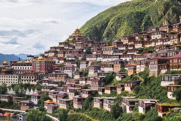 From below of row small wooden red houses randomly constructed on foot of tall slope covered with mountain forest