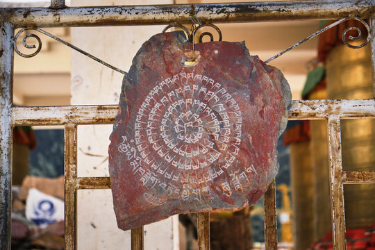 Mantra on old red square shabby stone slab on ground near pile of stones in yard of church