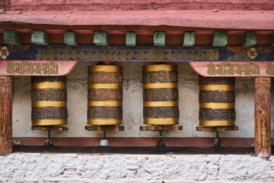 Exterior of Tibetan church decorated with big cylindrical rolls with stripes and hieroglyphs between red shabby columns