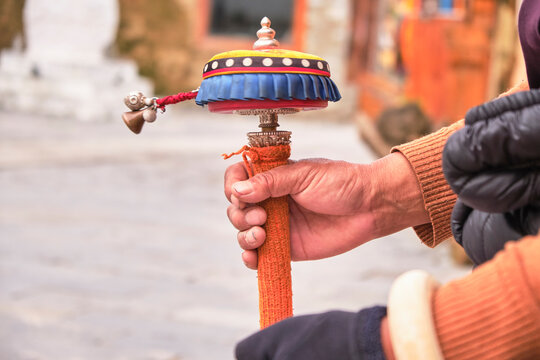 Unrecognizable buddhist rotating bright Tibetan roller while harmonizing energy and praying near blurred background of local oriental temple