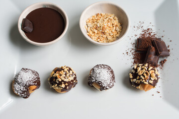 Presentation of delicious profiteroles with vanilla cream, chocolate sauce and hazelnut pieces.
