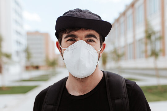 Anonymous Young Trendy Male In Face Mask And Cap Looking At Camera Near Buildings During COVID 19 Pandemic