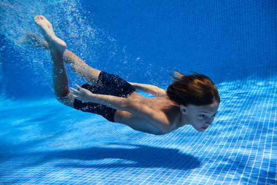 Underwater shot full body energetic teenage boy in swimming trunks diving into clean pool water in resort