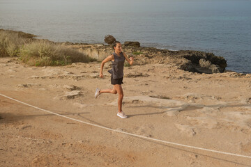 Young sporty athletic female in activewear running fast on empty shore with shrubs