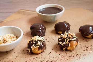 Presentation of delicious profiteroles with vanilla cream, chocolate sauce and hazelnut pieces.