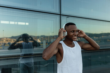 Cheerful African American male athlete smiling brightly while listening to music in wireless headphones during fitness training