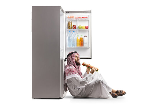 Arab Man Eating A Sandwich And Leaning On A Fridge