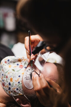 From above of crop anonymous master doing eyelash extension after mapping for unrecognizable female customer in face mask