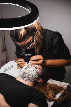 Female master doing eyelash extension after mapping for unrecognizable female customer in face mask