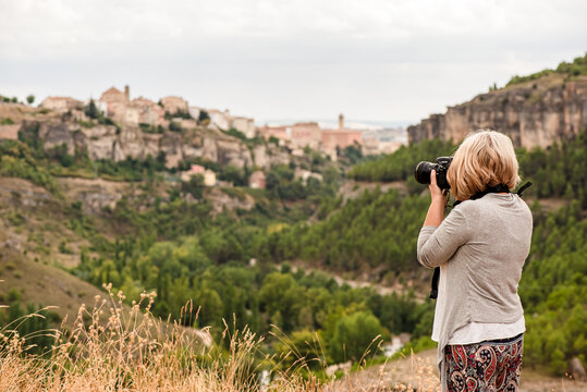 Side view of unrecognizable mature female photographer with professional photo camera taking pictures of old town Cuenca with medieval buildings on hill while traveling in Spain