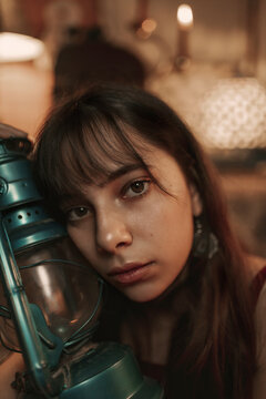 Peaceful female in red dress sitting in cozy room with old fashioned kerosene lantern while enjoying evening and looking at camera