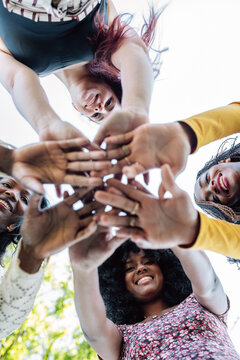 From below of group of multiracial cheerful women standing together and stacking hands in name of unity and friendship