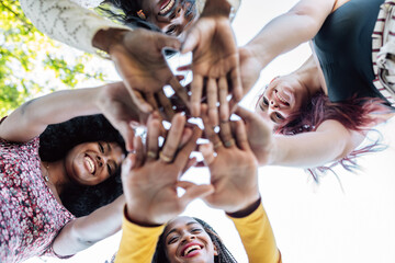 From below of group of multiracial cheerful women standing together and stacking hands in name of unity and friendship