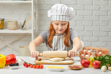 little child girl in chef hat and an apron rolled out the dough in the kitchen