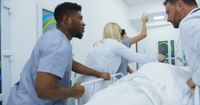 Emergency department. Rear of mixed-races doctors and nurses moving patient in oxygen mask lying on a hospital stretcher through hospital corridors. Coronavirus. Covid-19 concept. Medical rescue team