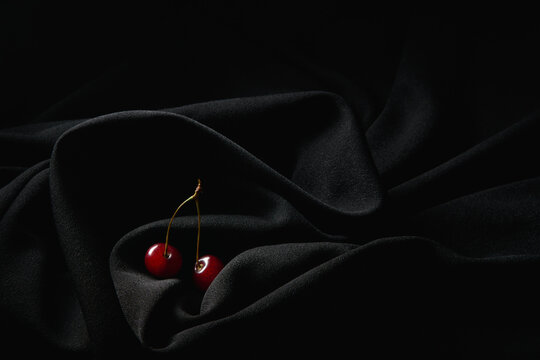 Red small cherries on thin stems placed on dark black wrinkled cloth in studio