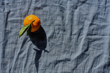 Tangerines or oranges, clementines,citrus fruits with green leaves on pastel blue textile...