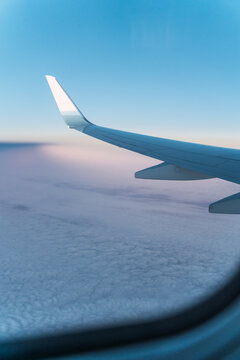 View of white wing of modern aircraft flying at sunrise over clouds against blue sky