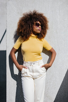 Black Woman With Afro Hair Posing In Front Of A Gray Wall Looking Away