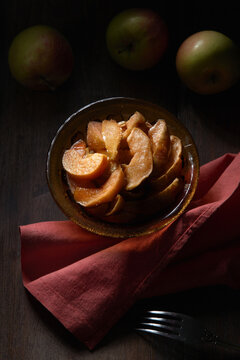 From above of bowl with delicious sweet sliced baked apples served on table with fork and napkin
