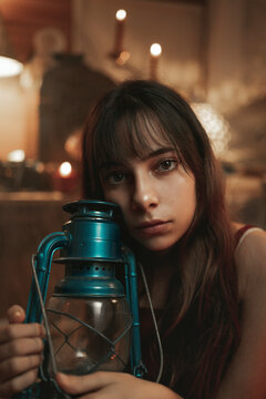 Peaceful female in red dress sitting in cozy room with old fashioned kerosene lantern while enjoying evening and looking at camera