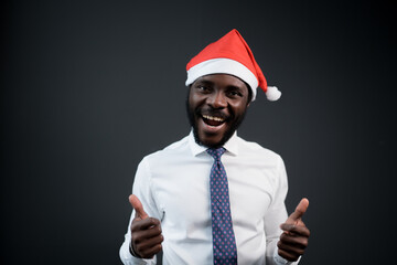 African american man in white shirt and tie with Santa hat on his head raises his thumb up and rejoices at christmas