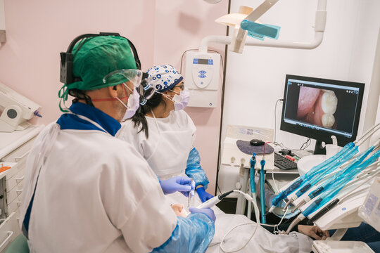 Back view of unrecognizable doctor and nurse in uniform near patient and desktop computer with dental image on screen in clinic