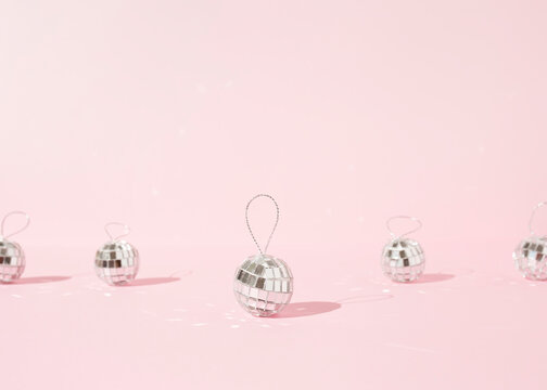 Shiny Christmas baubles in shape of disco balls placed on pink background in studio