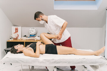 Side view of male therapist stretching legs of female patient lying on table during physiotherapy massage in clinic
