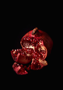 Fresh ripe halved pomegranate and seeds on black background