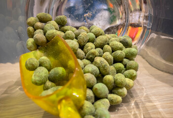 Close up of wasabi peanuts and a yellow plastic transparent measuring shovel  in a glass jar