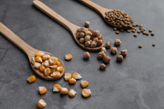 Top view of assorted dried ingredients placed in wooden spoons and scattered on black table in kitchen