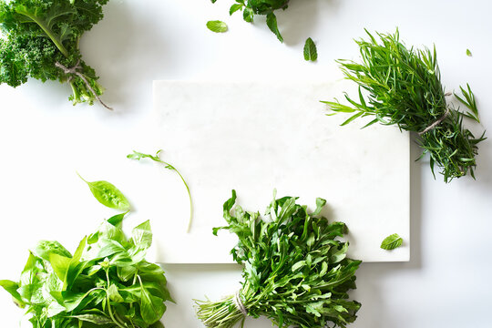 Flat lay with various herbs and lettuce and marble cutting board on white background