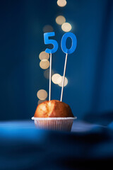 Birthday cupcake or muffin with number fifty (50) and lights on the blue background. Birthday or...