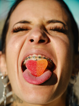 Closeup of eccentric female with braces and closed eyes holding sweet gummy candy on stuck out tongue
