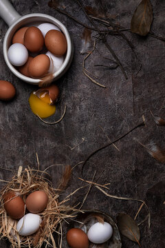 Top view of cracked and whole chicken eggs of white and brown colors arranged on messy surface with feathers