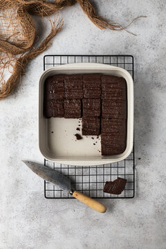 Top view of ceramic baking pan with traditional brownie cake cut into pieces placed on metal grid with knife on kitchen table