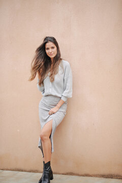 Charming female with long hair and in casual dress standing near building on street and modestly looking at camera