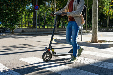 Side view of cropped unrecognizable black male riding modern scooter in city while commuting to work on sunny day in summer