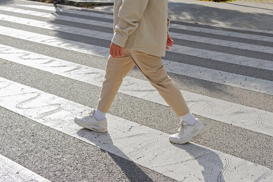 Cropped unrecognizable male pedestrian wearing casual outfit crossing on zebra crosswalk on the street on sunny day