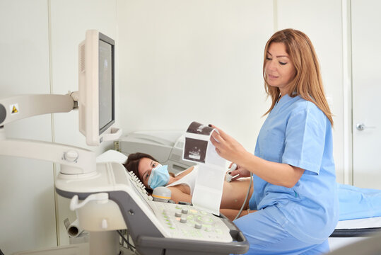 Female medic checking ultrasound pictures near professional equipment and anonymous patient during sonography diagnostic in clinic